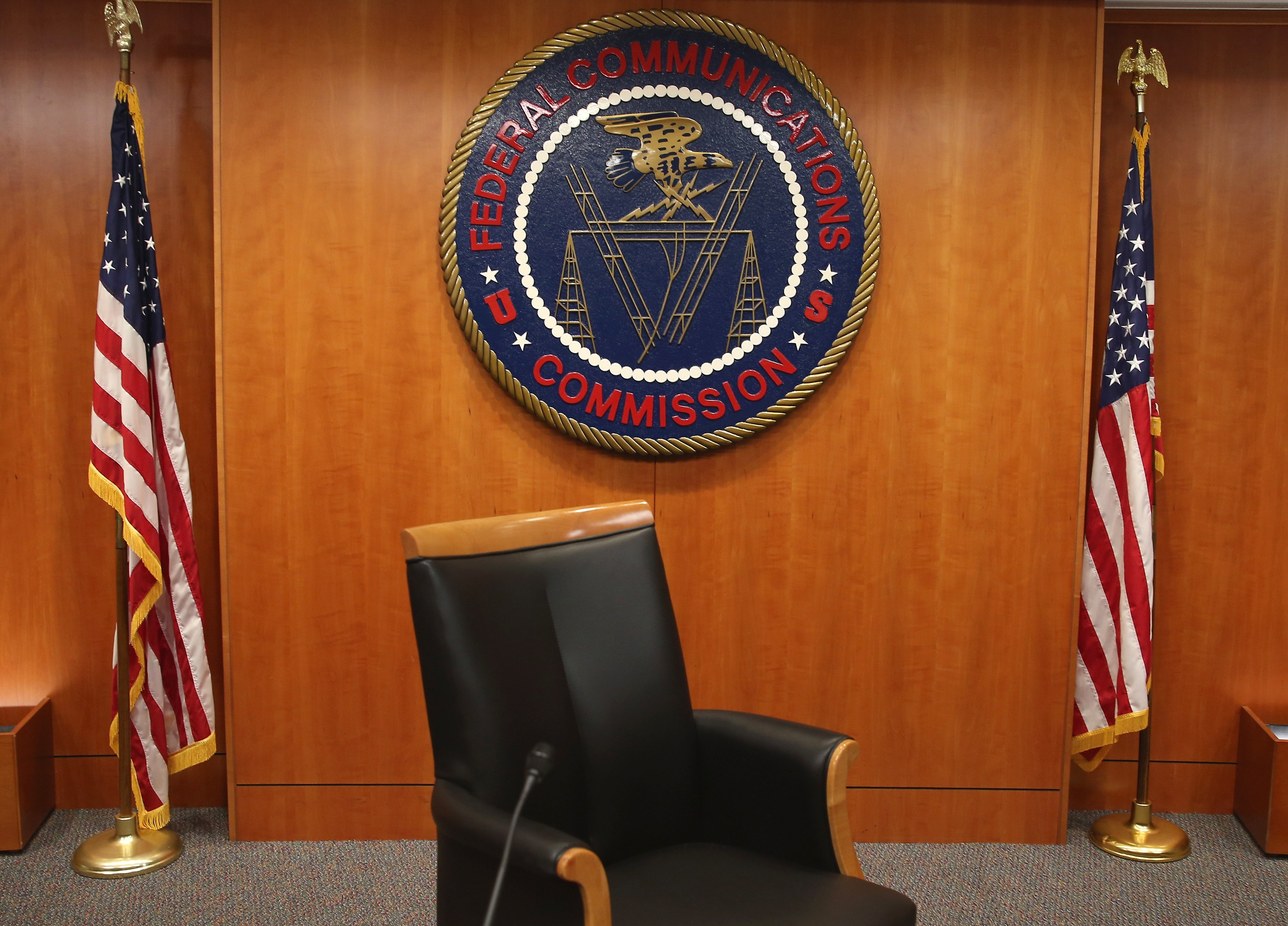 The seal of the Federal Communications Commission hangs between two American flags; the FCC is urging broadcasters to air more "patriotic" content in the run-up to the country
